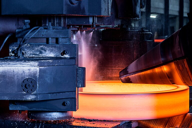 Close up of manufacturing machine shaping red hot steel ring in foundry